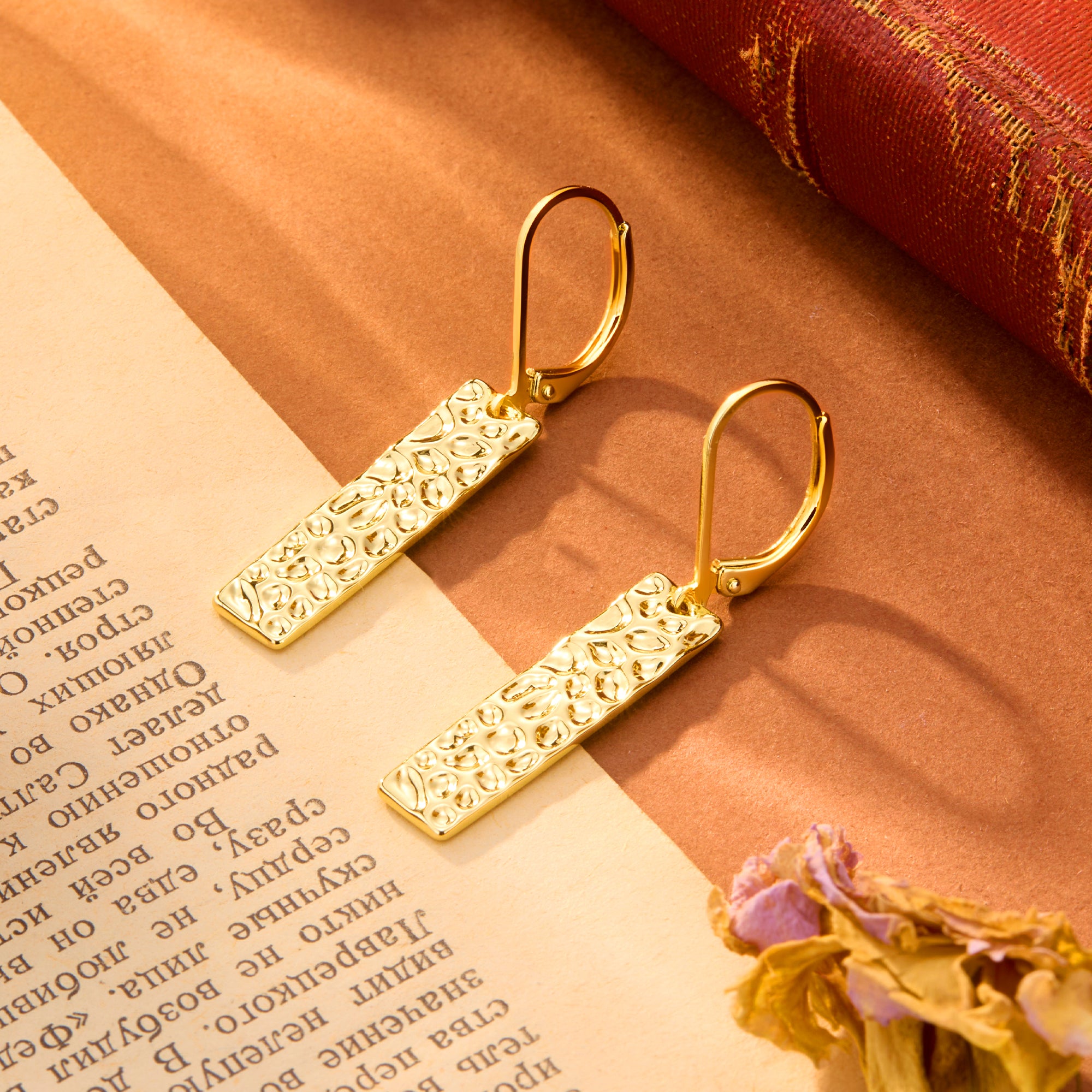 Gold-tone hammered rectangular bar dangle earrings, close-up on textured surface