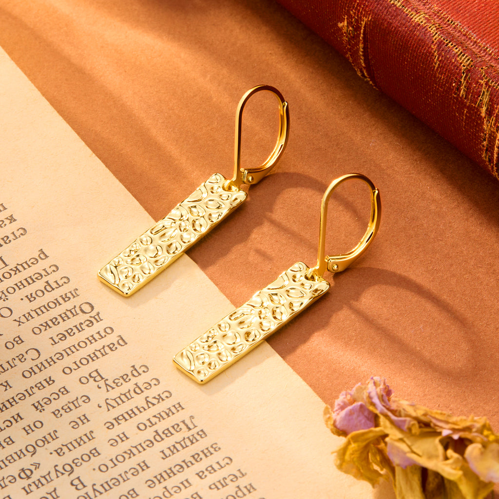 Gold-tone hammered rectangular bar dangle earrings, close-up on textured surface