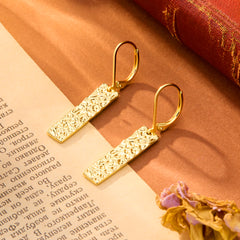 Gold-tone hammered rectangular bar dangle earrings, close-up on textured surface
