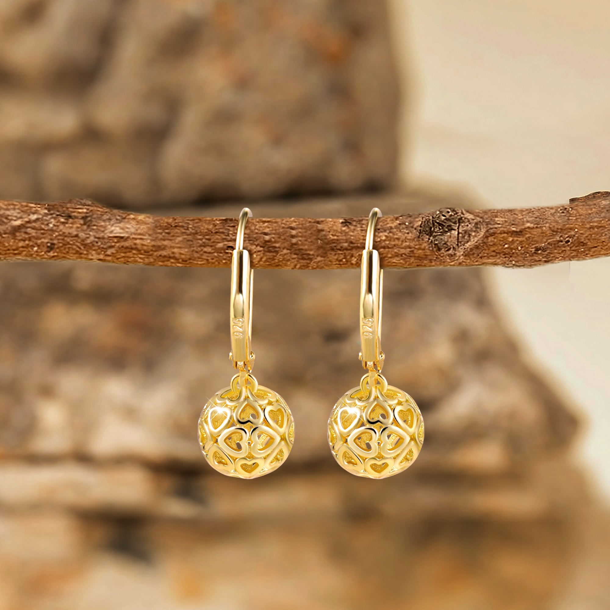 Gold hoop-style lever drop earrings with heart-pattern round skeleton ball charm