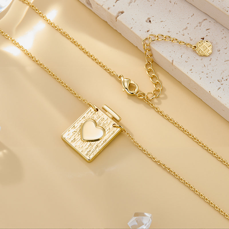 Gold heart locket pendant with textured square face and heart inset, includes small chain charm.