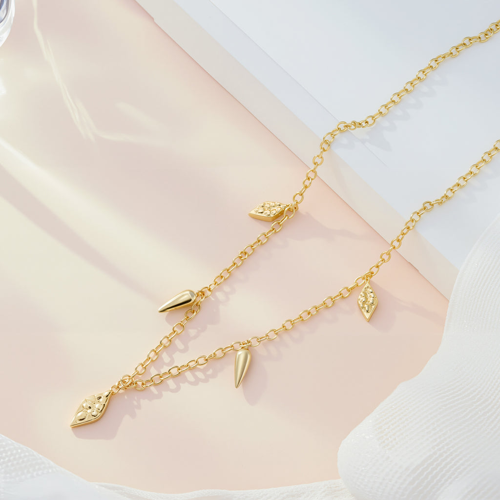 Gold geometric drop necklace flat lay with cone and teardrop charm dangles