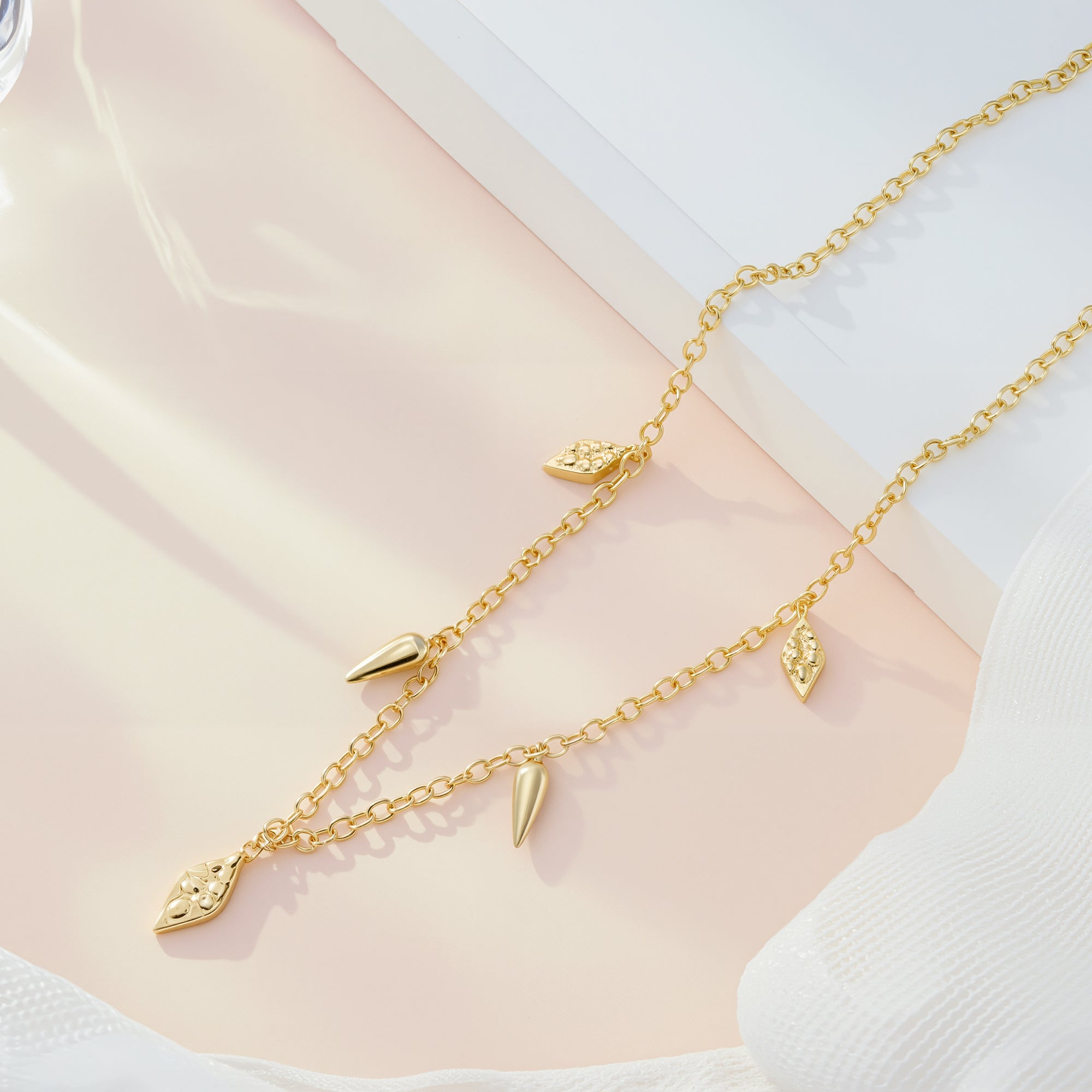Gold geometric drop necklace flat lay with cone and teardrop charm dangles