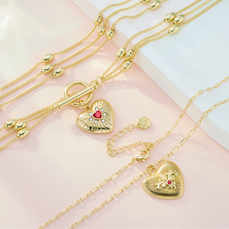 Gold heart pendant necklace with layered paperclip chains and red gemstone center