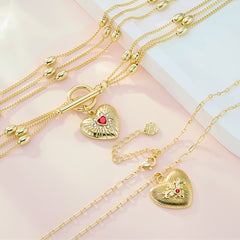 Gold heart pendant necklace with layered paperclip chains and red gemstone center