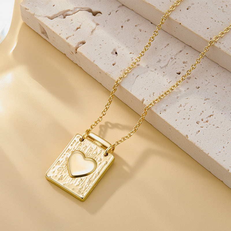 Gold textured square heart locket pendant on chain, heart emblem set in the front.