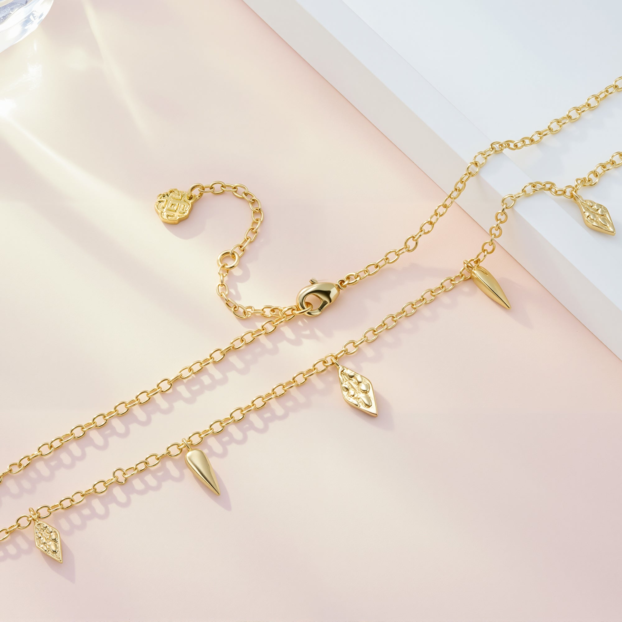 Gold geometric drop necklace showing textured center charm and cone teardrop dangles