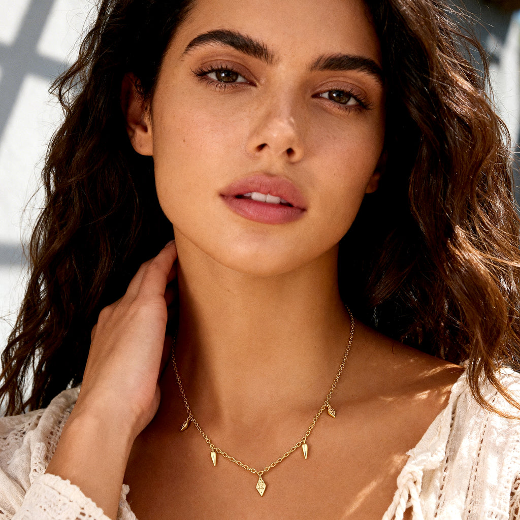 Gold geometric drop necklace on model, with small spike and teardrop charms
