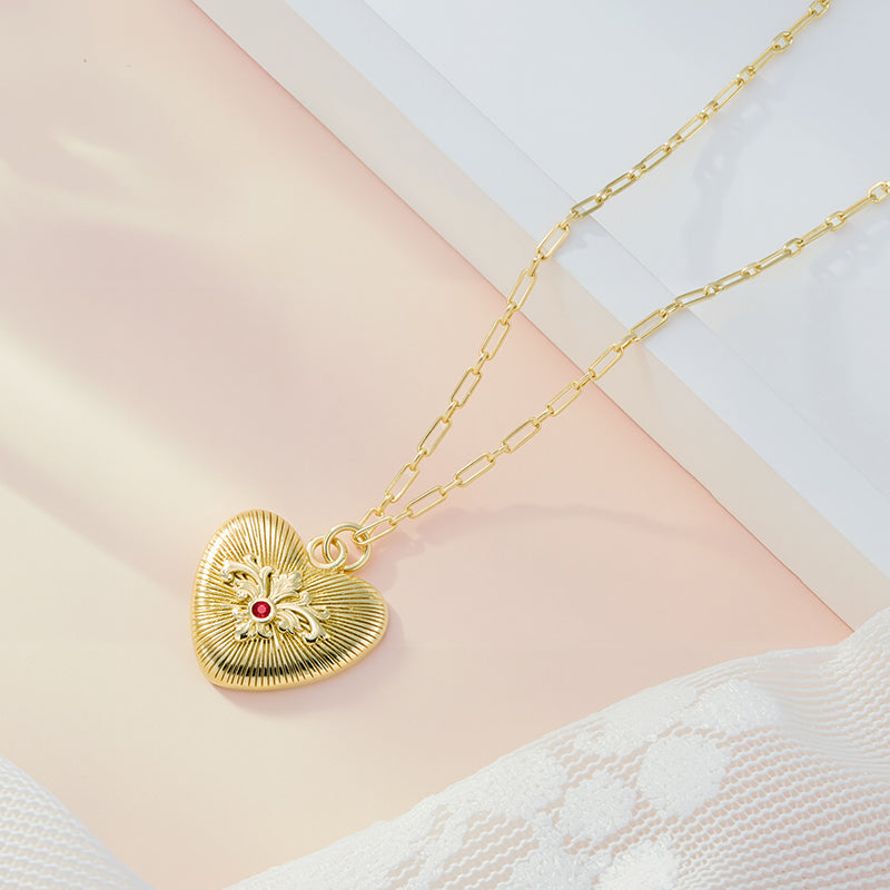 Gold heart pendant on chain with sunburst embossing and red gemstone center