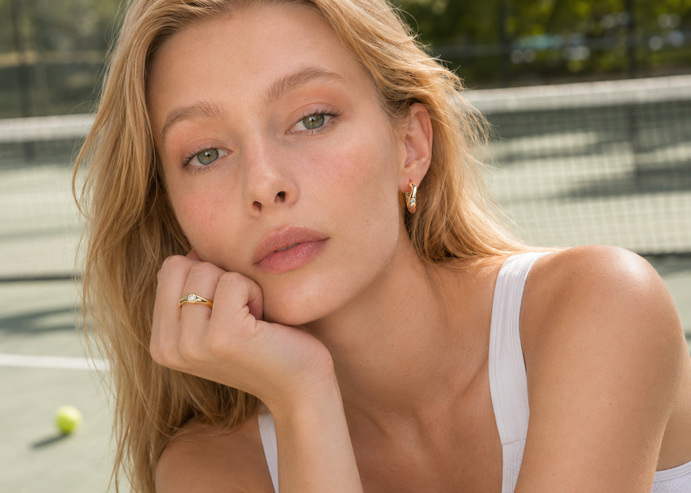 Model wearing gold-plated jewelry on a tennis court